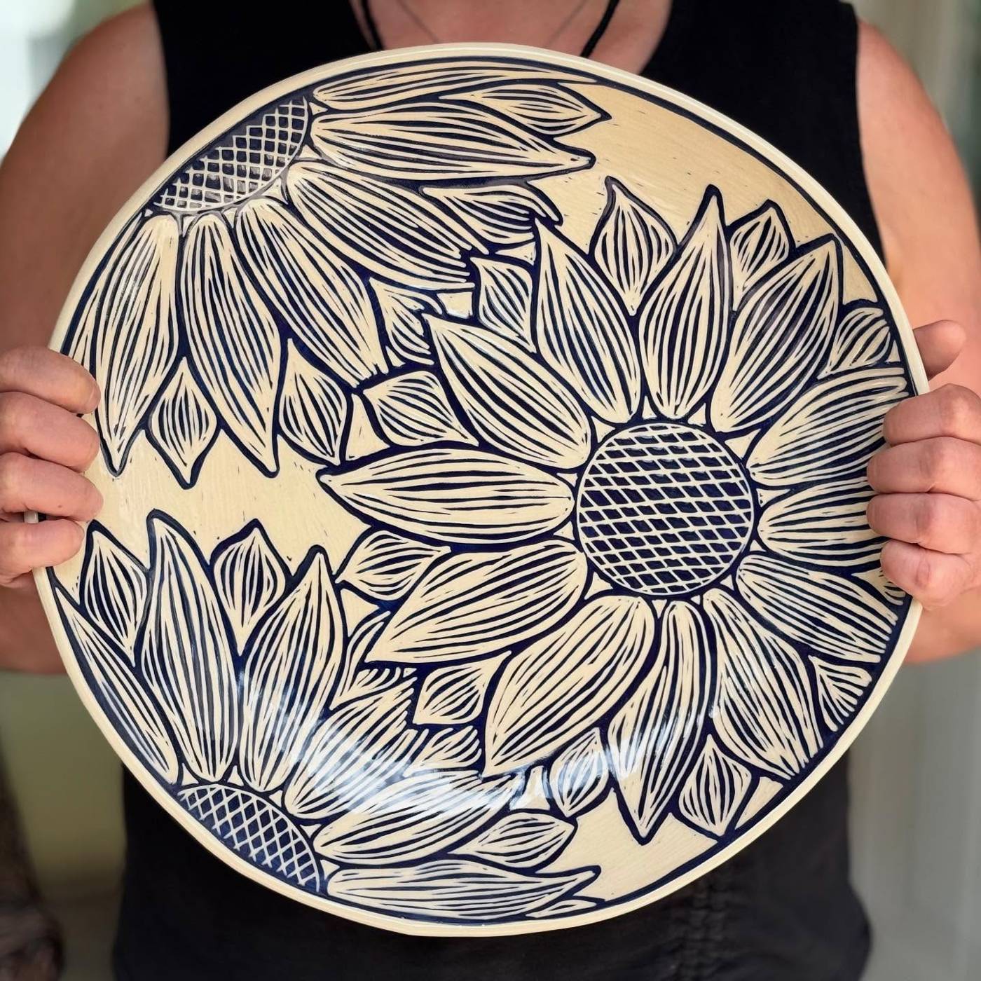 Hands holding up a large carved sunflower platter